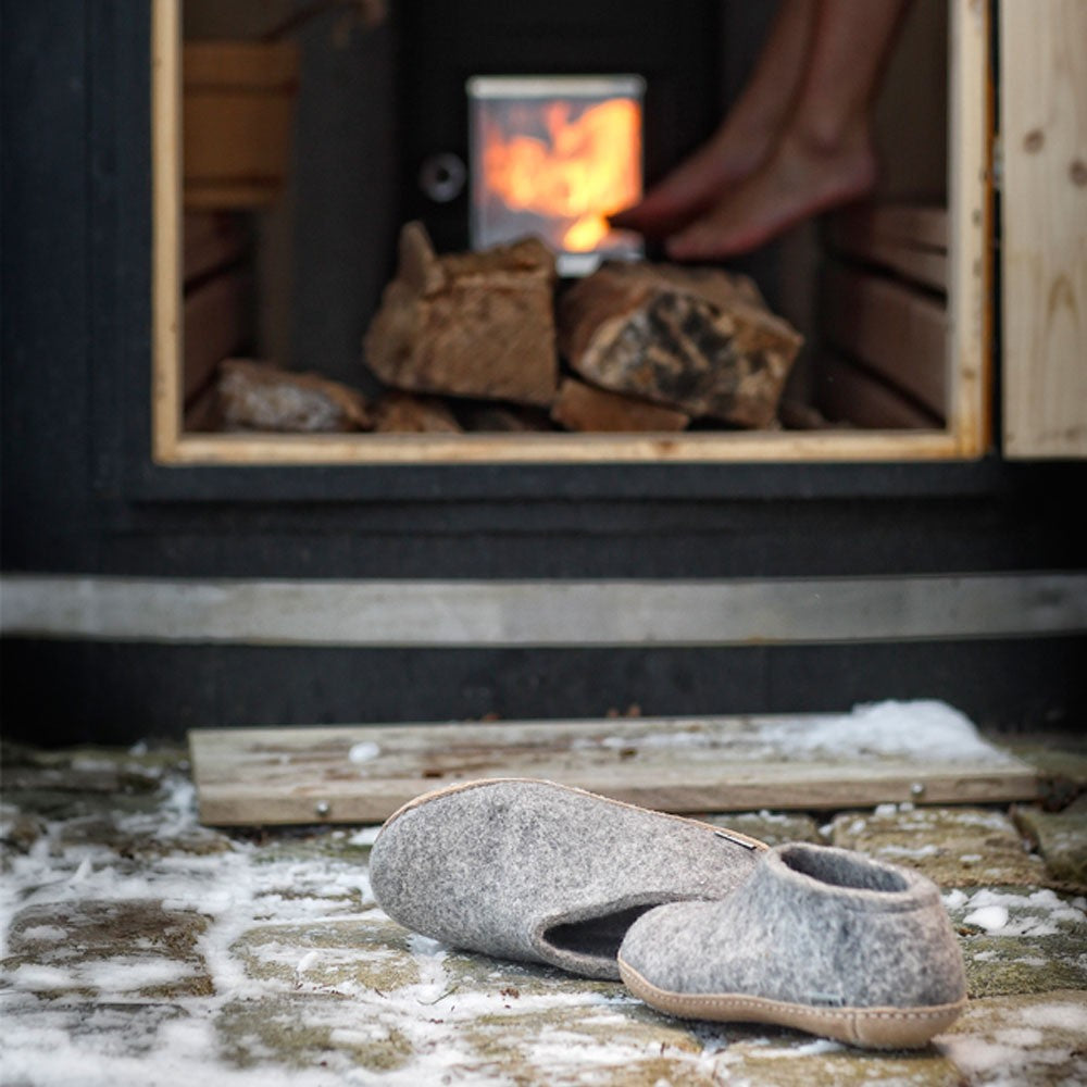 A pair of soft soled grey glerups shoes sit outside a sauna on a winters day