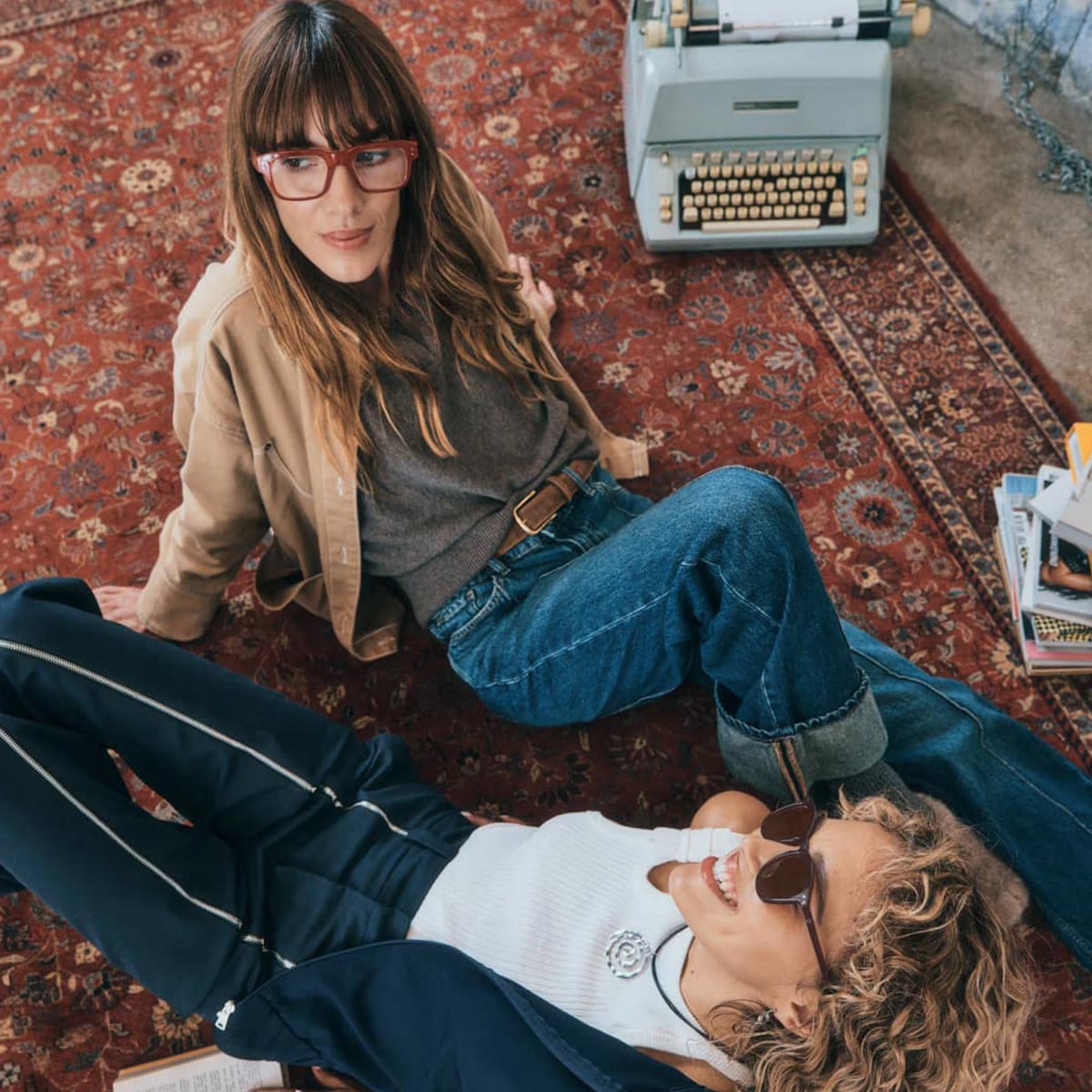 Two people wearing Izipizi glasses sitting on a patterned rug with a typewriter in the background