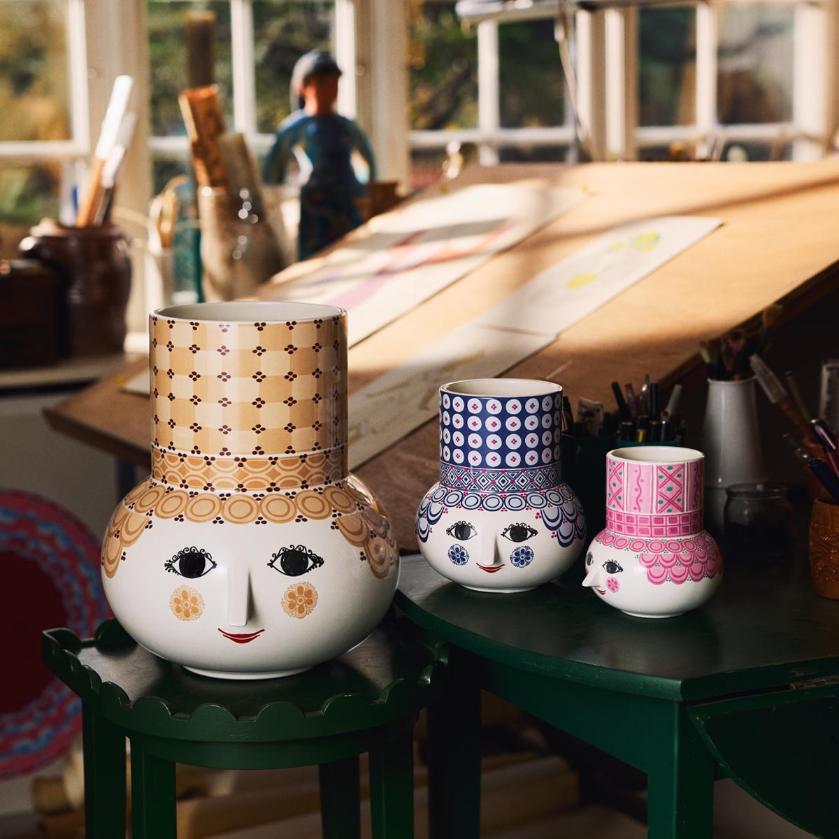 Three decorative Bjørn Wiinblad Olga vases with face designs on a table in a workshop setting.
