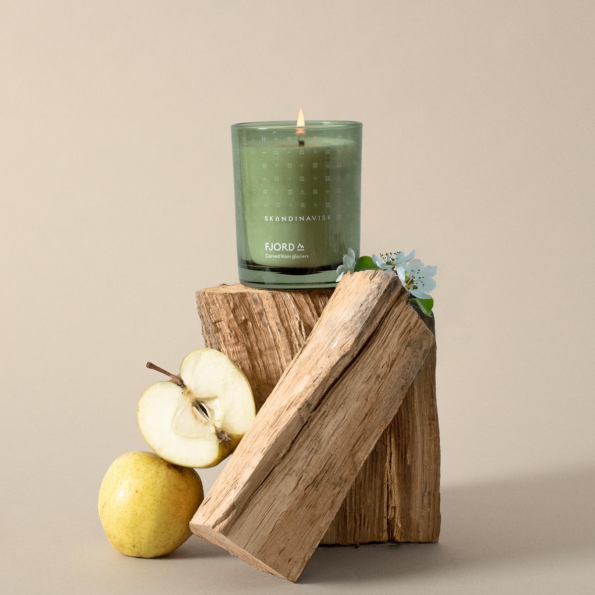 Green Skandinavisk Fjord candle on a wooden block with apples and flowers on a beige background