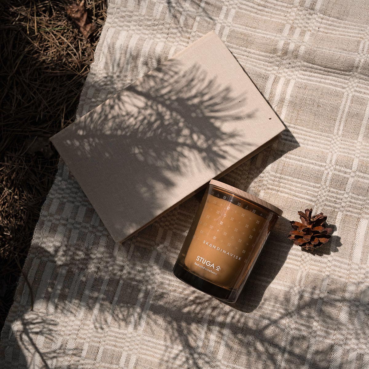 Stuga Candle with a pine cone on a textured surface, casting shadows