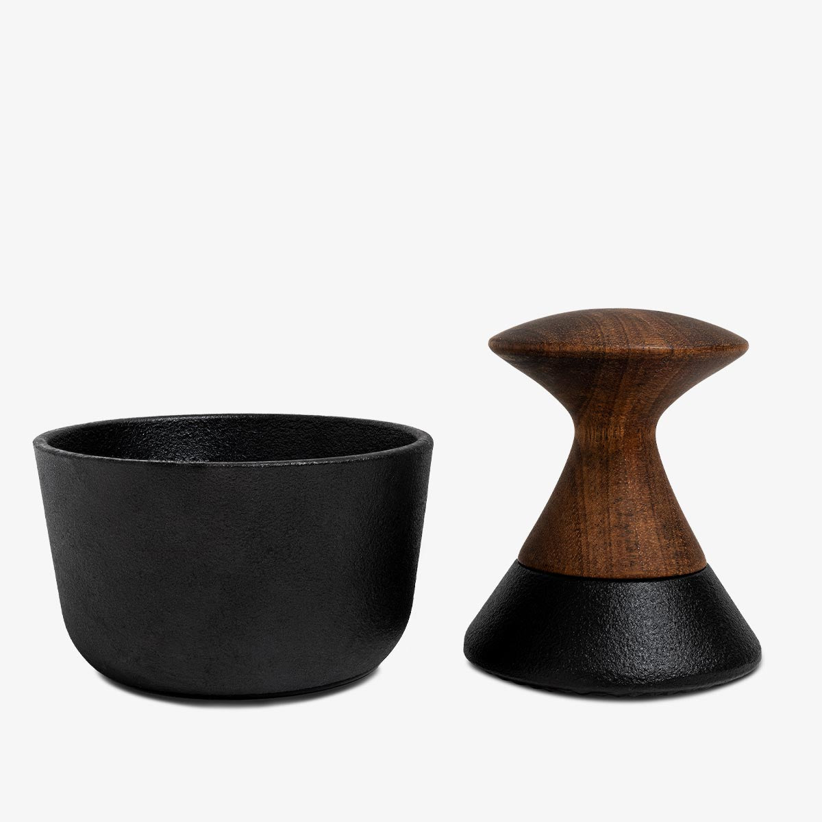 Black Crushgrind metal mortar and wooden pestle next to each other on a white background