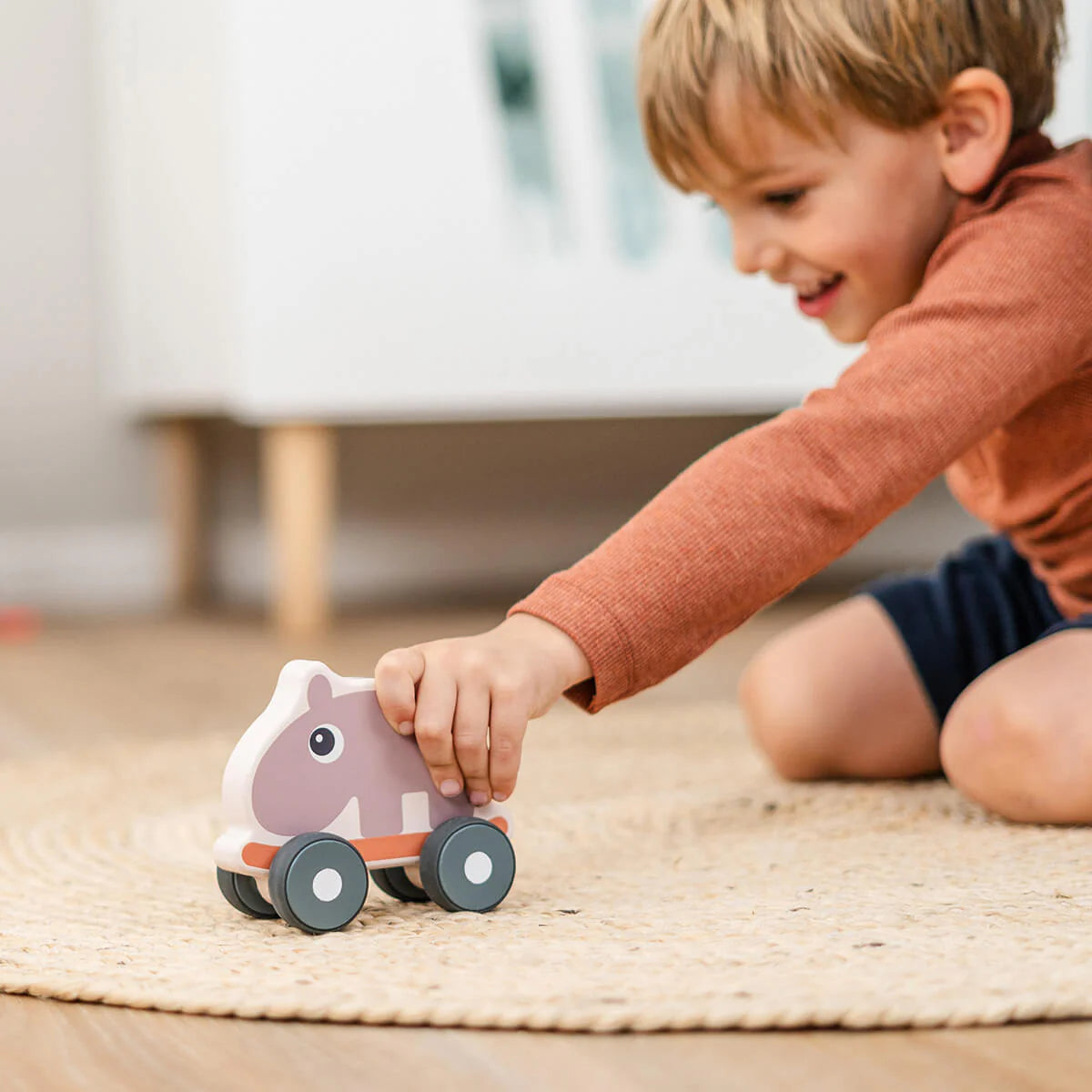 Child playing with a Done by Deer 'Ozzo' Push Toy on a rug set on a wooden floor.