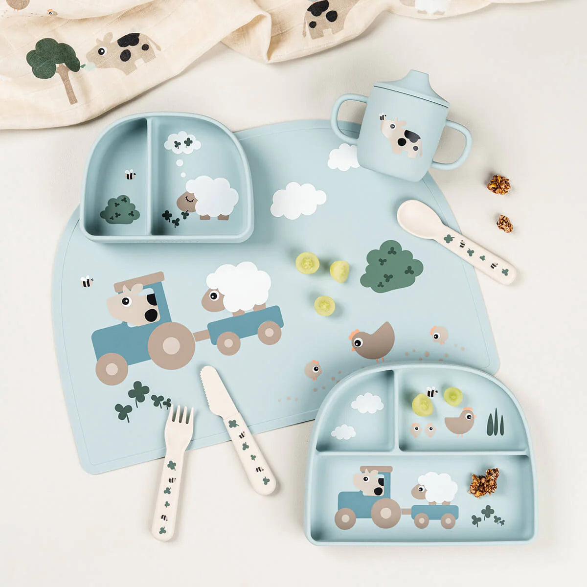 Image taken from above of a collection of Done by Deer tableware in light blue scattered on a light coloured table with snacks and a muslin cloth.