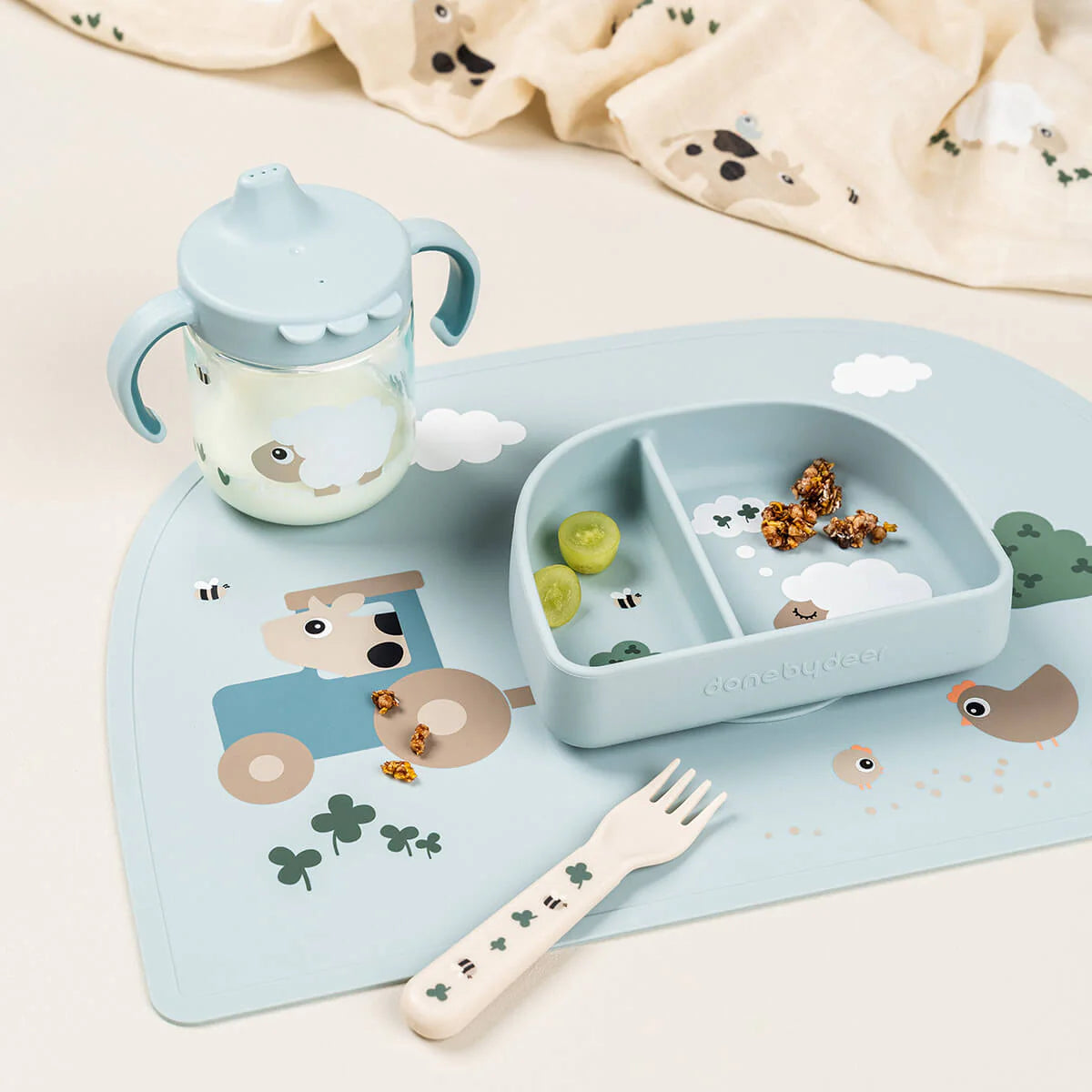 A collection of Done by Deer tableware in blue scattered on a light coloured table with snack pieces and a muslin cloth.