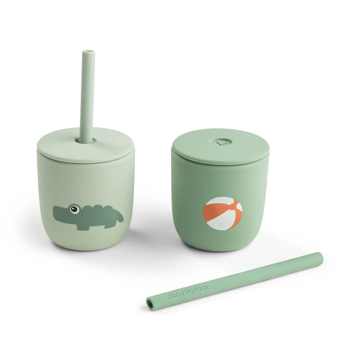 Two green silicone straw cups by Done by Deer set against a white background with one straw lying on its side.