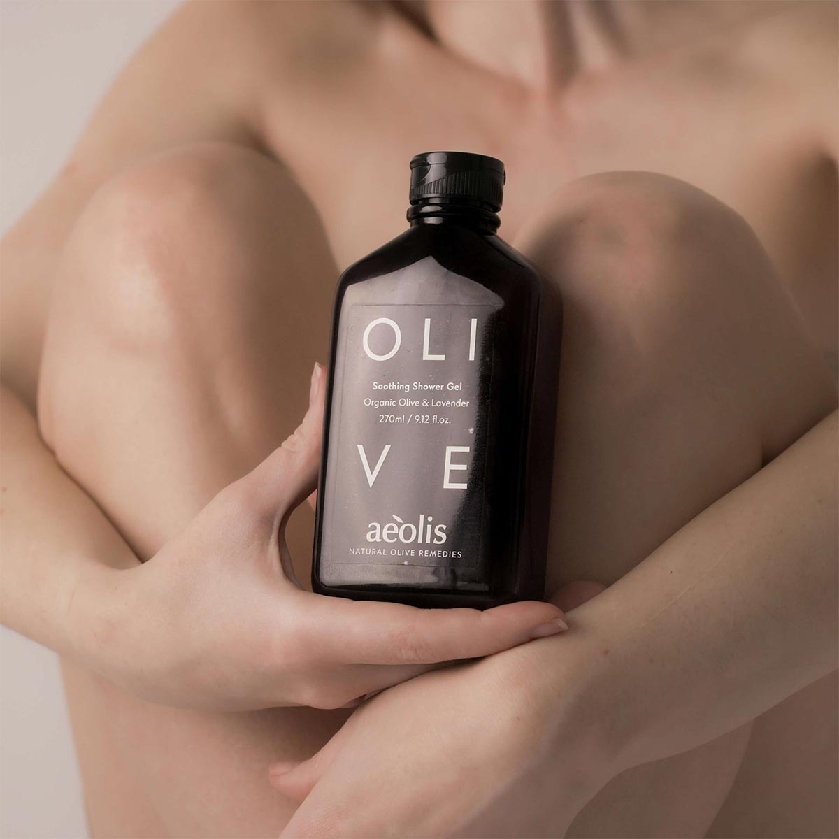 Person holding a bottle of 'aeolis' olive shower gel with a blurred background