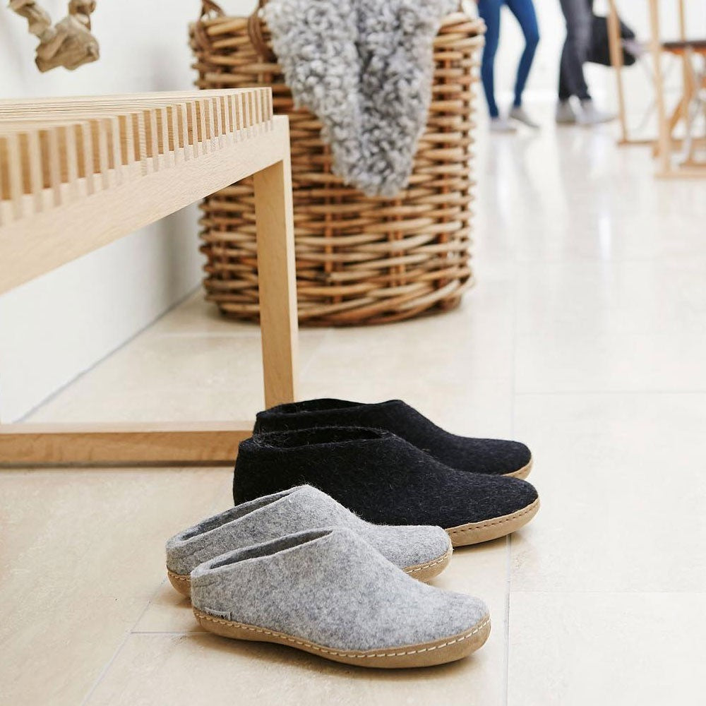 A pair of grey leather soled Glerups mules sit on the floor of a Nordic styled room