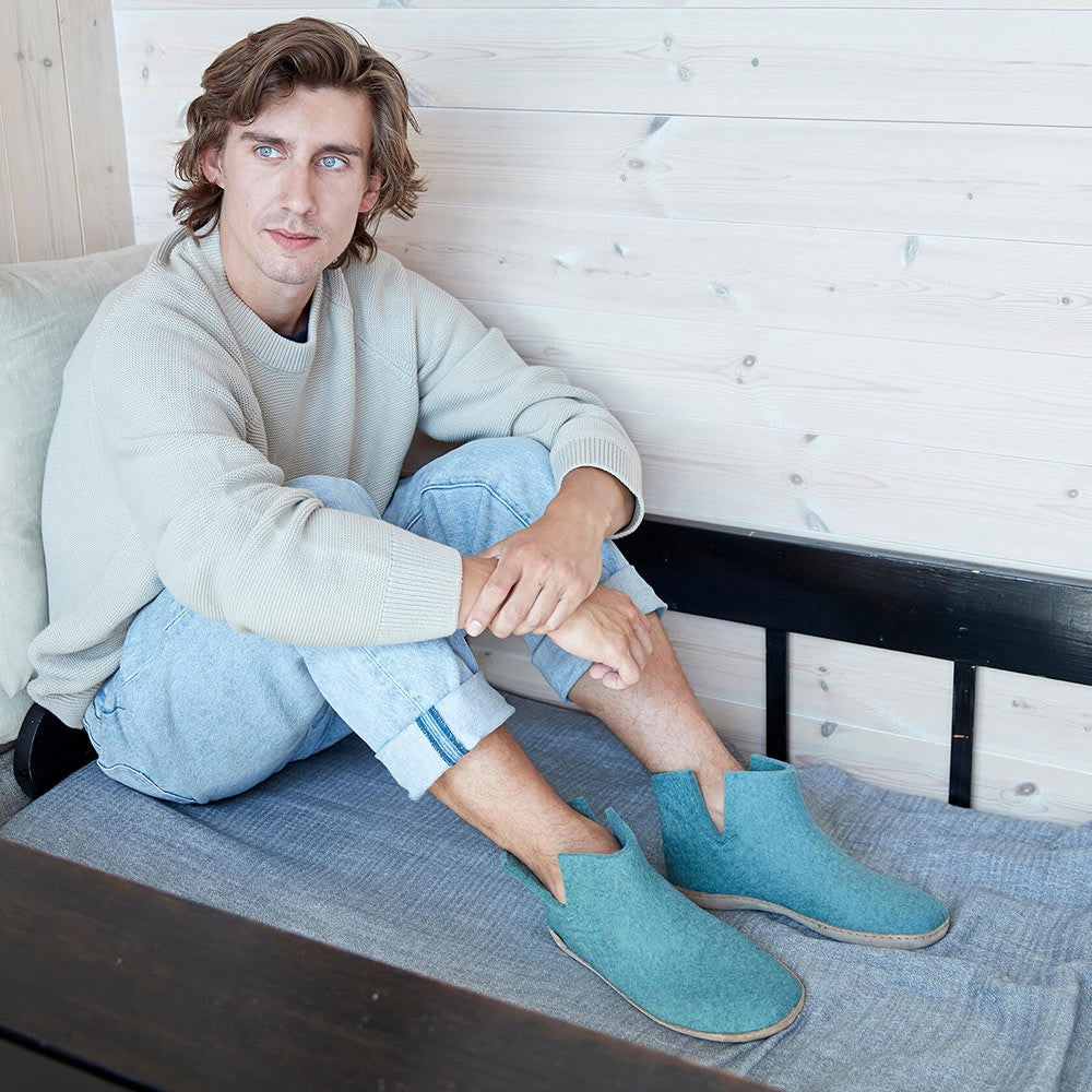 A man sits wearing a pair of Glerups North Sea boots with natural leather soles