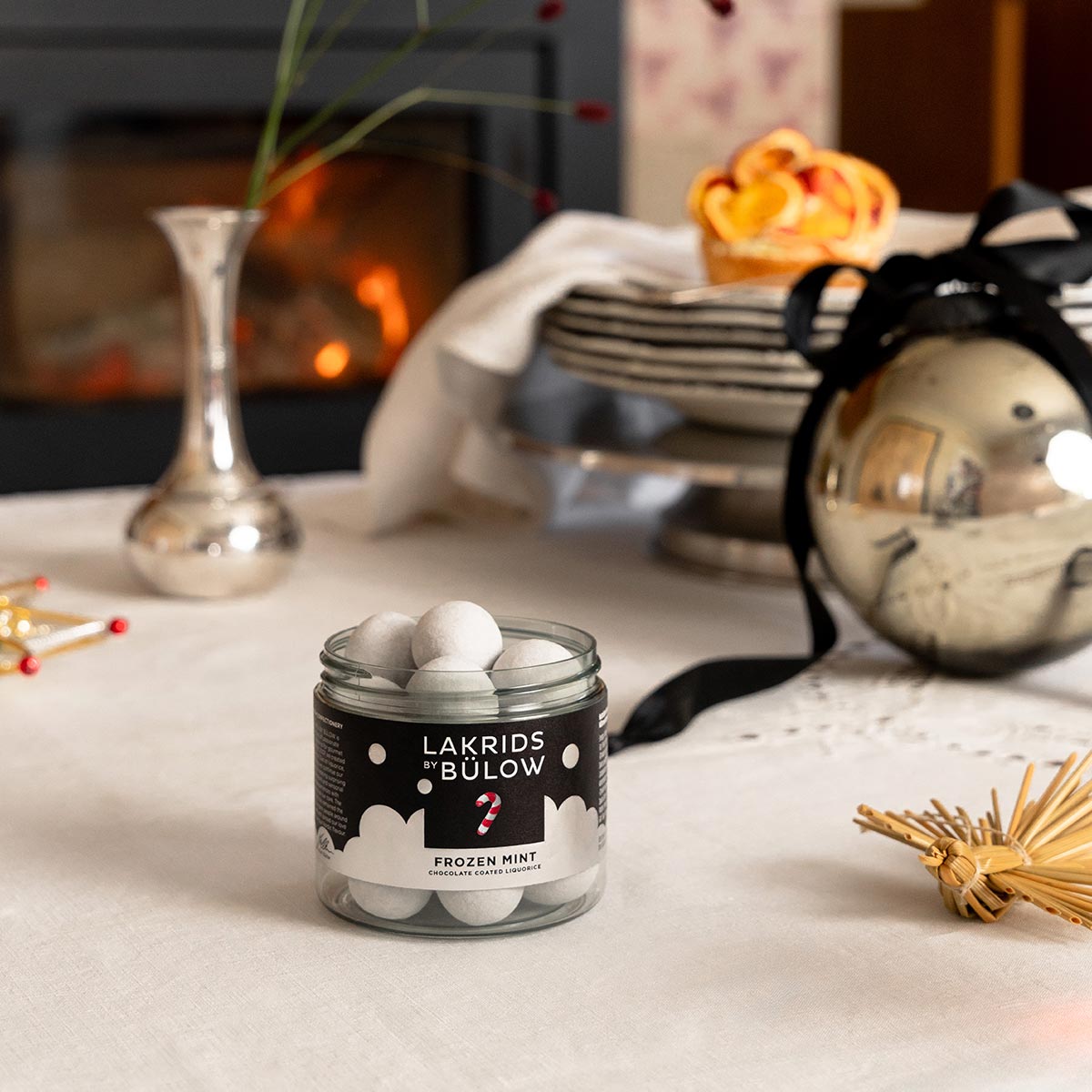 Jar of Lakrids Bülow Frozen Mint chocolate coated liquorice on a table with festive decorations in the background.