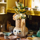 Decorative Bjørn Wiinblad  Olga sand vase with face design and floral arrangement on a table with various ceramic items.
