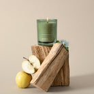 Green Skandinavisk Fjord candle on a wooden block with apples and flowers on a beige background