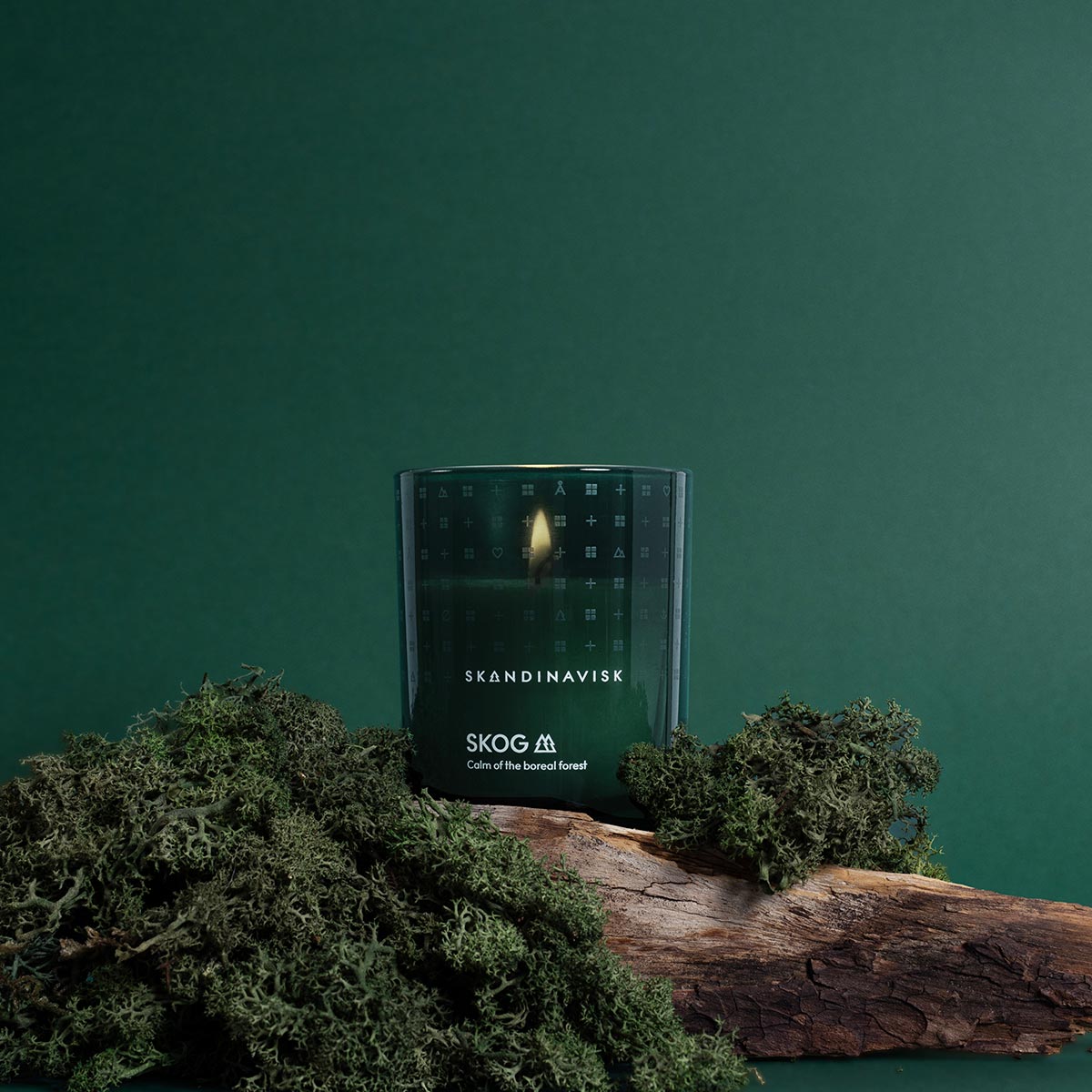 Skandinavisk Skog candle on a wooden log with green foliage against a green background