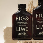 Two bottles of Fig & Lime body lotion by aeolis on a textured beige background