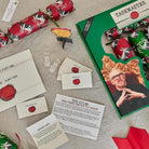 Taskmaster Game components including cards, envelopes, and a box with a person's face on it, on a textured surface.