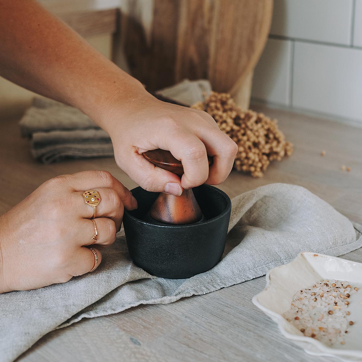 Person using a Crushgrind mortar and pestle to grind salt on a kitchen counter with ingredients and a towel.