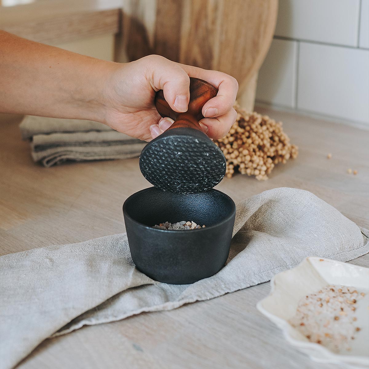 Person using a Crushgrind pestle and mortar to grind salt on a kitchen counter with a neutral background