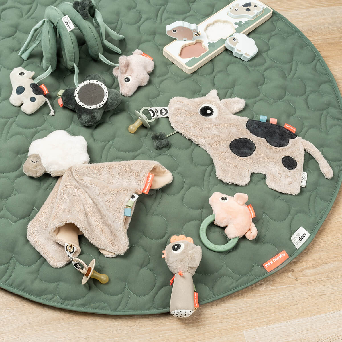 Green mat on a wooden floor with Done by Deer products scattered across it including the 'Sheepy' comfort blanket with a pacifier attached.