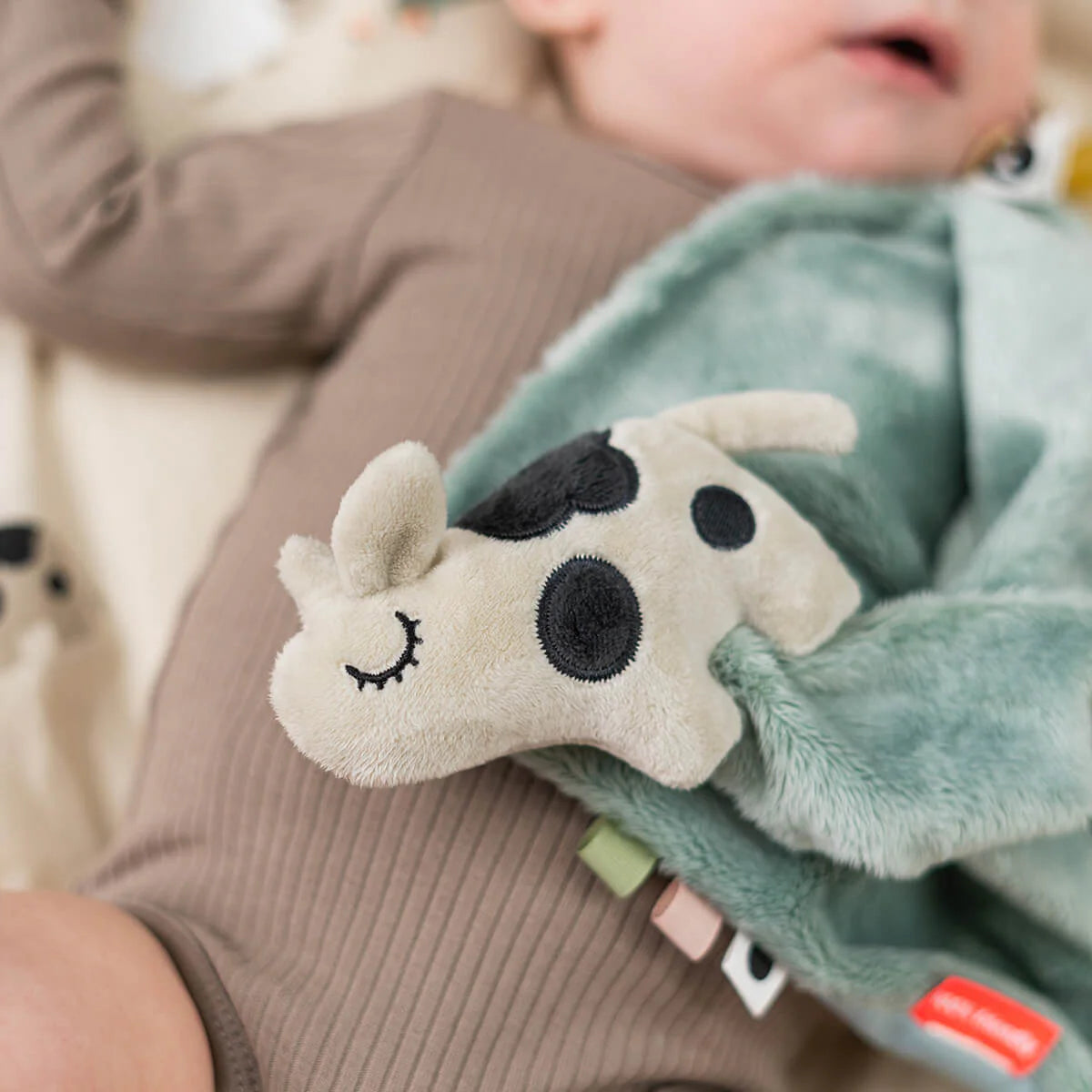 Baby lying on a blanket with Done by Deer 'Dotti' comfort blanket with pacifier attachment.