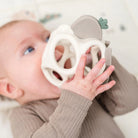 Baby lying on a white blanket holding Done by Seer 'Sheepy' grip and teether toy.