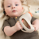 Baby lying on a beige blanket holding the Done by Deer 'Clucky' teether rattle.