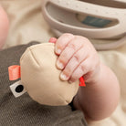 Child's hand holding the egg rattle from Done by Deer 'Clucky' teether rattle with the teether part of the toy shown in the background.