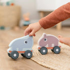 Child's hand reaching for two Done by Deer push toys on a wooden floor with a rug.