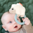 image from above of baby holding a 'Sheepy' sensory rattle and teether whilst lying on a green quilt.