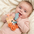 Baby holding a Done by Deer activity ring in 'Celebration' design on a beige patterned blanket.