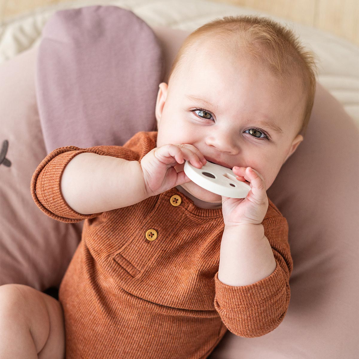 Baby in a brown outfit holding the teething part of 'Ozzo' Done by Deer Grip Toy, against a neutral background.