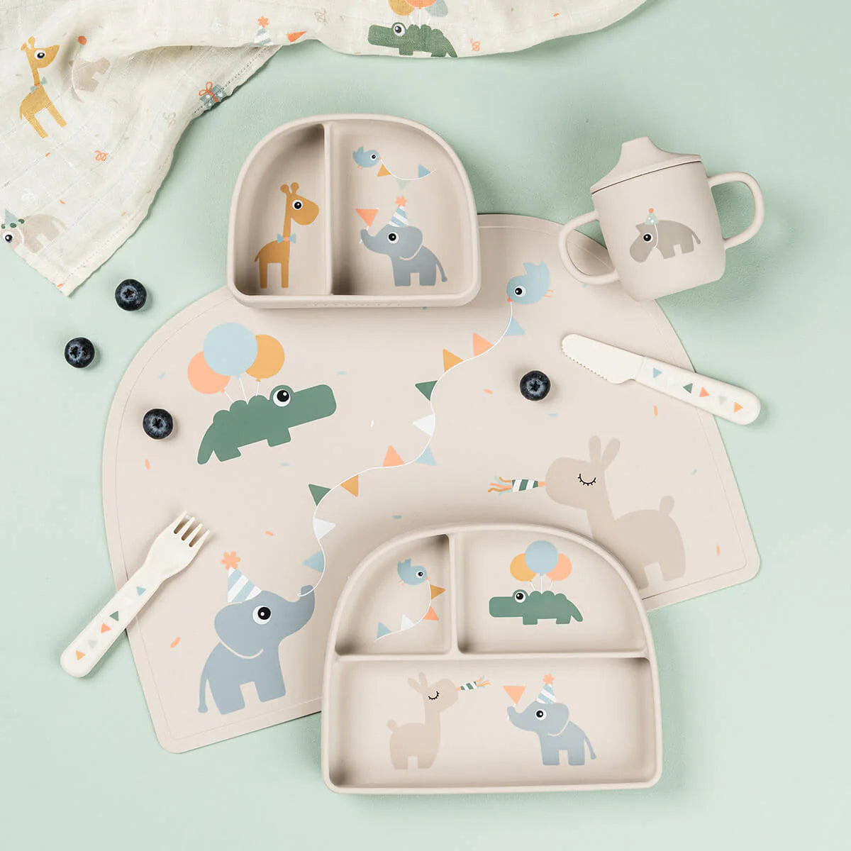A collection of Done by Deer tableware in the colour 'sand' scattered on a light coloured table with blueberries and a muslin cloth.