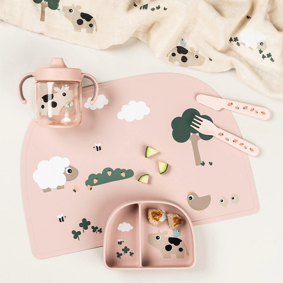 A collection of Done by Deer tableware in powder pink scattered on a light coloured table with snack pieces and a muslin cloth.