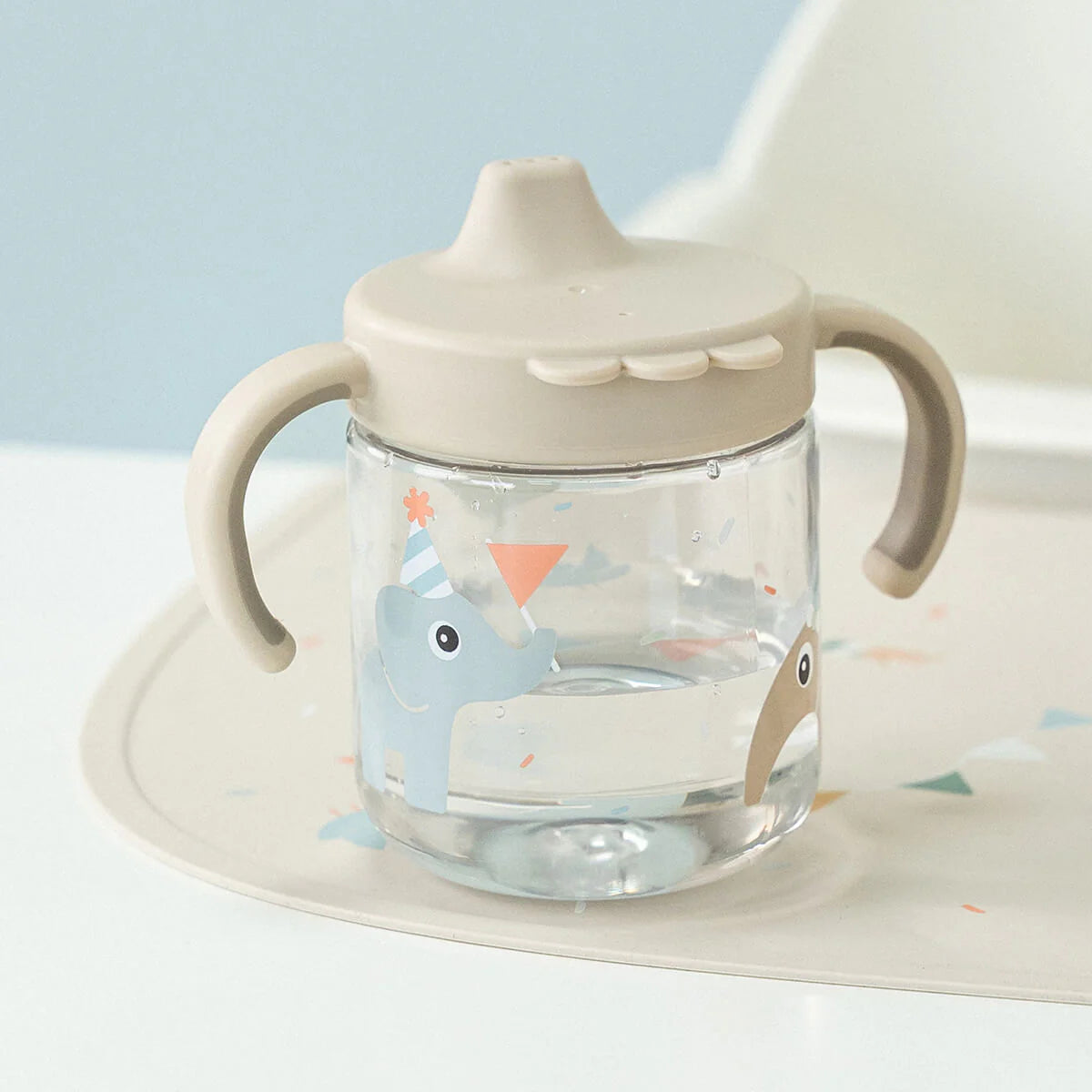 Done by Deer grippy spout cup filled with water in 'sand' colour on a highchair against a light blue background.