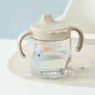 Done by Deer grippy spout cup filled with water in 'sand' colour on a highchair against a light blue background.