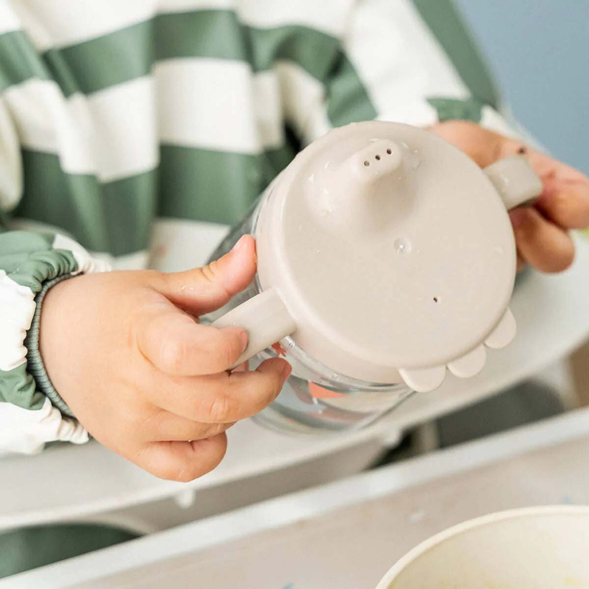 Child's hands holding a grippy spout cup by Done by Deer.