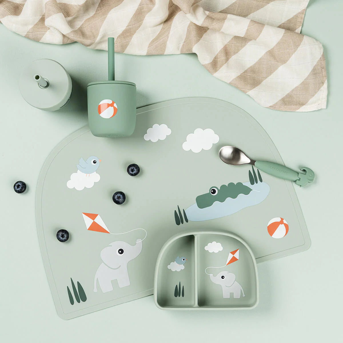 A collection of Done by Deer tableware in mint green scattered on a light coloured table with blueberries and a muslin cloth.