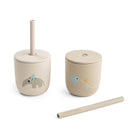 Two beige silicone straw cups by Done by Deer set against a white background with one straw lying on its side.