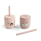 Two pale pink silicone straw cups by Done by Deer set against a white background with one straw lying on its side.