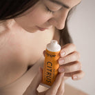 Woman holding a tube of 'aeolis' Citrus product close to her face.