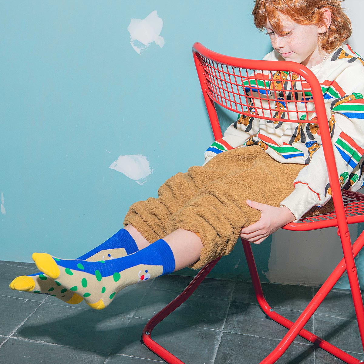child sitting on a red chair wearing Eat My Socks Happy Dog socks