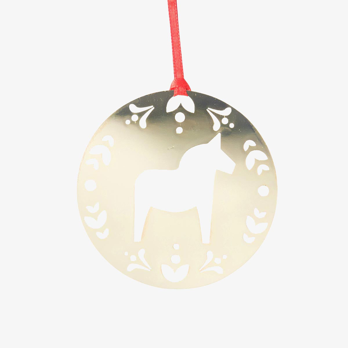 A round, metallic gold Christmas ornament featuring a white silhouette of a Dala horse in the center, surrounded by decorative cutout patterns, hanging from a red string against a light gray background.