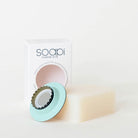 Soapi Starter Kit featuring a pale cream bar of soap, a mint green circular soap dish with a dark metal bottle top, and the white product box in the background.