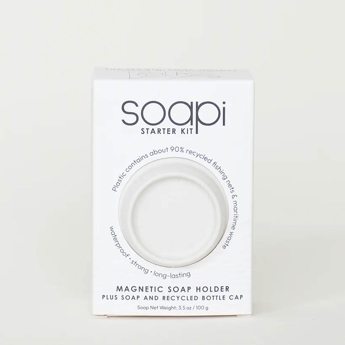 A white rectangular product box for the Soapi Starter Kit, featuring a circular cutout window that reveals a white magnetic soap holder inside. The packaging text highlights recycled fishing net and marine wax materials, and lists the product as a magnetic soap holder plus soap and recycled bottle cap.
